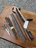 Top view of all tools laid out on a wooden surface showing scissors, large metal iron bar with holes, curved metal tool, long metal rasp with plastic handle, and small metal grater.