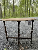Front view of solid wood hall table showing three turned legs and horizontal stretcher support, placed outdoors on gravel.