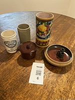Overview photo showing all five pottery vessels on a wooden surface, including the colorful fruit motif vase, brown covered pot, three hole beige piece, green vase, and marked beige vessel.