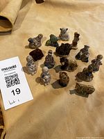 Photo showing entire lot of 15 small ceramic Wade figurines arranged on a tan surface, with visible figures including animals and character shapes.
