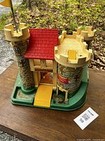 Front view of vintage Fisher Price castle toy showing red roof, stone tower walls, yellow drawbridge on green base