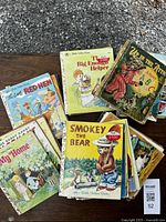 35 vintage Little Golden Books with colorful illustrated covers, stacked and spread for display, showing titles including The Big Enotzy Helper, Smokey the Bear, The Saggy Baggy Elephant, The Little Red Hen, The Zip-It Alphabet, My Home, and others, with visible wear and age.