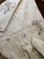 Full view of the white quilt showing hand-stitched embroidery with floral vase designs and general condition including holes and wear.