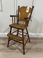 Front left angle view of the vintage wooden toddler chair, showing the seat, backrest, armrests, footrest, and legs.