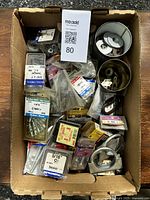 Box filled with various hardware items including metal washers, small metal clips, metal wall anchors, and packaged screws and nails.