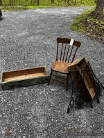 Wide view of all items showing wood chair, drawers, and sewing machine iron ends on gravel.