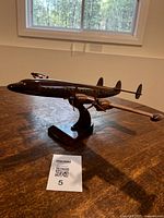 Side view of the dark polished wooden model airplane on a stand, showing detailed propellers and yellow window accents.