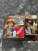 Top view of workshop lot showing safety glasses, respirator masks, funnels, tape, and assorted small items in boxes arranged on wooden surface.