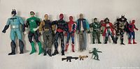 Full front view of ten action figures arranged in a row on a flat light background with some small accessories in front of them.