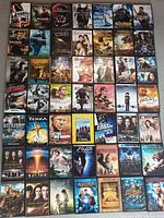 Photo showing a wide full view of multiple DVD covers laid out flat, titles including Bourne series, Fast & Furious series, Dune, Twilight, The Dark Tower, and various action and sci-fi movies.
