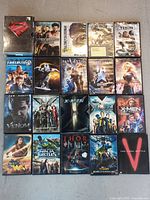 Photo showing 20 DVD cases laid out on the floor featuring superhero and comic book movies including Superman, X-Men, Thor, Fantastic Four, and more.