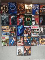 Photo showing a collection of 26 DVD boxsets and collections laid out, mostly featuring sci-fi and fantasy series like Stargate SG-1, Smallville, Star Wars, and more.