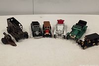 Front view of all toy vehicles and the toy cannon showing seven classic toy cars and one toy cannon on white surface