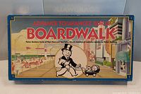 Photo of front lid showing colorful artwork of Mr. Monopoly and boardwalk scene with bright reds, blues, and yellows.