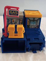 Front view showing the gas station signpost, yellow fuel pumps, and illustrated store windows on a blue playset.