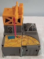 Side and top views of a vintage G1 Transformers Ironworks playset with yellow crane, red hook, and grey base with graphic details.