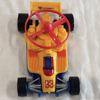 Front view of yellow racing toy car with red steering wheel, number 93 on front, and Autobot insignia on rear spoiler.