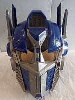 Front view of the Optimus Prime helmet showing the molded faceplate, blue and silver coloring, and symbols on the sides.