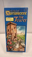 Front view of Carcassonne The Tower Expansion 4 box showing knight in armor on horse beside stone tower in countryside.