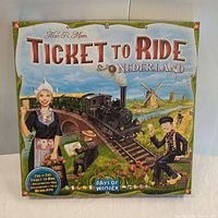Closed box of Ticket to Ride Nederland board game showing Dutch countryside artwork with a steam train and traditional clothing figures
