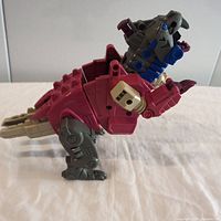 Side view of the vintage Hasbro Transformers G1 Grotesque figure showing pinkish-red body sections with gray legs, tail, and head featuring blue details.