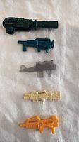 Five different color Hasbro Transformers G1 weapon accessories laid flat on a white surface