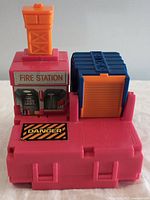 Front view of the fire station playset showing orange tower, red base with Danger decal, blue garage door, and Fire Station sticker.
