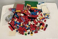 Photo showing collection of vintage Lego bricks in various colors along with multiple baseplates and some small parts spread out on white surface.