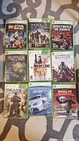 Photo showing 9 Xbox 360 game cases laid out on carpet, titles visible including LEGO Star Wars, Halo Reach, Brothers in Arms, Bioshock, Spec Ops, Assassin's Creed II, Gears of War 3, Need for Speed Shift, Kung Fu Panda.