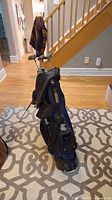 Full view of Cleveland golf bag standing upright indoors on patterned carpet near stairs.