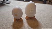Two egg-shaped kitchen items on the floor: one is a timer with eyes and orange feet, the other is a larger plain egg with orange feet.