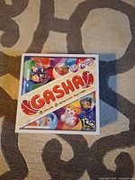 Flat photo of closed Gasha game box with colorful cartoon-style characters and logos on top.