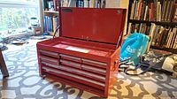 Front view of red tool chest with top lid open showing multiple small drawers in the front and inner compartment.