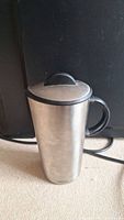 Metal pitcher with lid on, showing brushed metal finish and black handle.