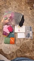 Plastic bags containing multiple colors of wool for felting and a foam pad with a needle inserted, along with a small white box and clear plastic case with felting needles and tools.