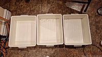 Top view of three white plastic storage bins placed side by side on the floor.