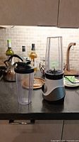 Photo of the blender base with tall blending container and separate travel top container with lid on counter.