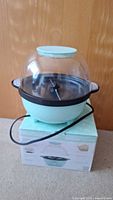 Elite Gourmet popcorn maker on top of original branded box with cord wrapped around base, clear dome lid on top