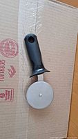Photo of pizza cutter showing black plastic handle and round stainless steel cutting blade.