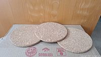 Three round cork trivets arranged side by side on a cardboard box with wooden background
