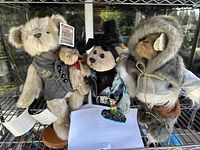 Three collectible teddy bears with distinct outfits displayed on a metal shelf.