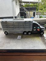 Side view of the black and grey toy truck showing the transparent multi-compartment cargo section and orange flame decal on the black cab.