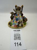 Front view of resin figurine showing mouse sitting on chair sewing patchwork quilt, with two smaller mice and yarn basket on a circular base.