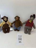 Photo showing three small bear collectibles with unique clothing including a brown one with tan jacket and goggles, a brown one with blue shorts, and a gray one with red vest and hat.