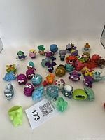 Several colorful Moshi collectible monster figures displayed on a white background, showing variety in color and design including purple, blue, green, orange, and silver figures with unique shapes and details