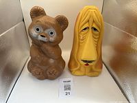 Both plastic animal figurines — brown bear and yellow dog — displayed side by side on white surface with tag visible.
