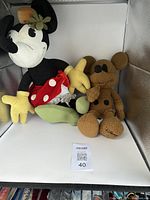 Photo showing both plush dolls in the lot; Minnie Mouse on the left with red polka dot skirt and green flower, Mickey Mouse on the right in brown textured fabric