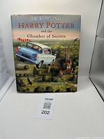 Front cover of the Harry Potter and the Chamber of Secrets hardcover book, showing detailed illustration of a flying blue car over a rural area with a tower.