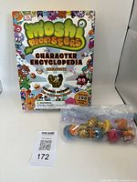 Front view of Moshi Monsters Character Encyclopedia book with the collectible Colonel Catcher figure in clear packaging placed in front.