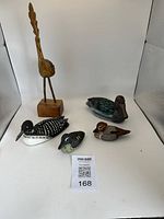 Five carved wooden bird figures in a white lightbox background, showing all items with different shapes and color patterns.